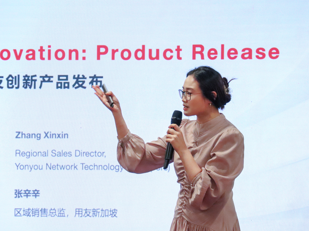 Zhang Xinxin, Regional Sales Director of Yonyou Network Technology (Singapore), presenting on stage to Yonyou’s existing customers. The backdrop displays a PowerPoint slide highlighting the features and functionalities of Yonyou’s products, demonstrating their potential for enhancing business operations.