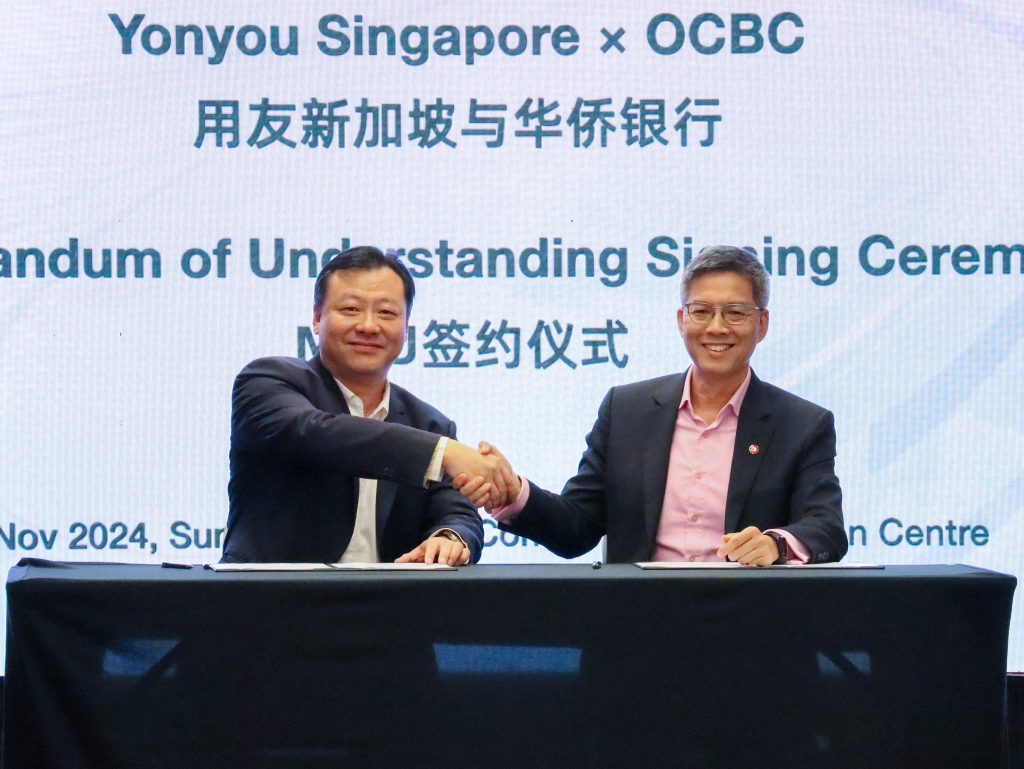 Howard Chen, Managing Director of Yonyou Network Technology (Singapore), and Roy Tan, Head of Enterprise Banking International, Global Commercial Banking, OCBC, shaking hands in a celebratory gesture following the successful collaboration, both smiling in agreement.