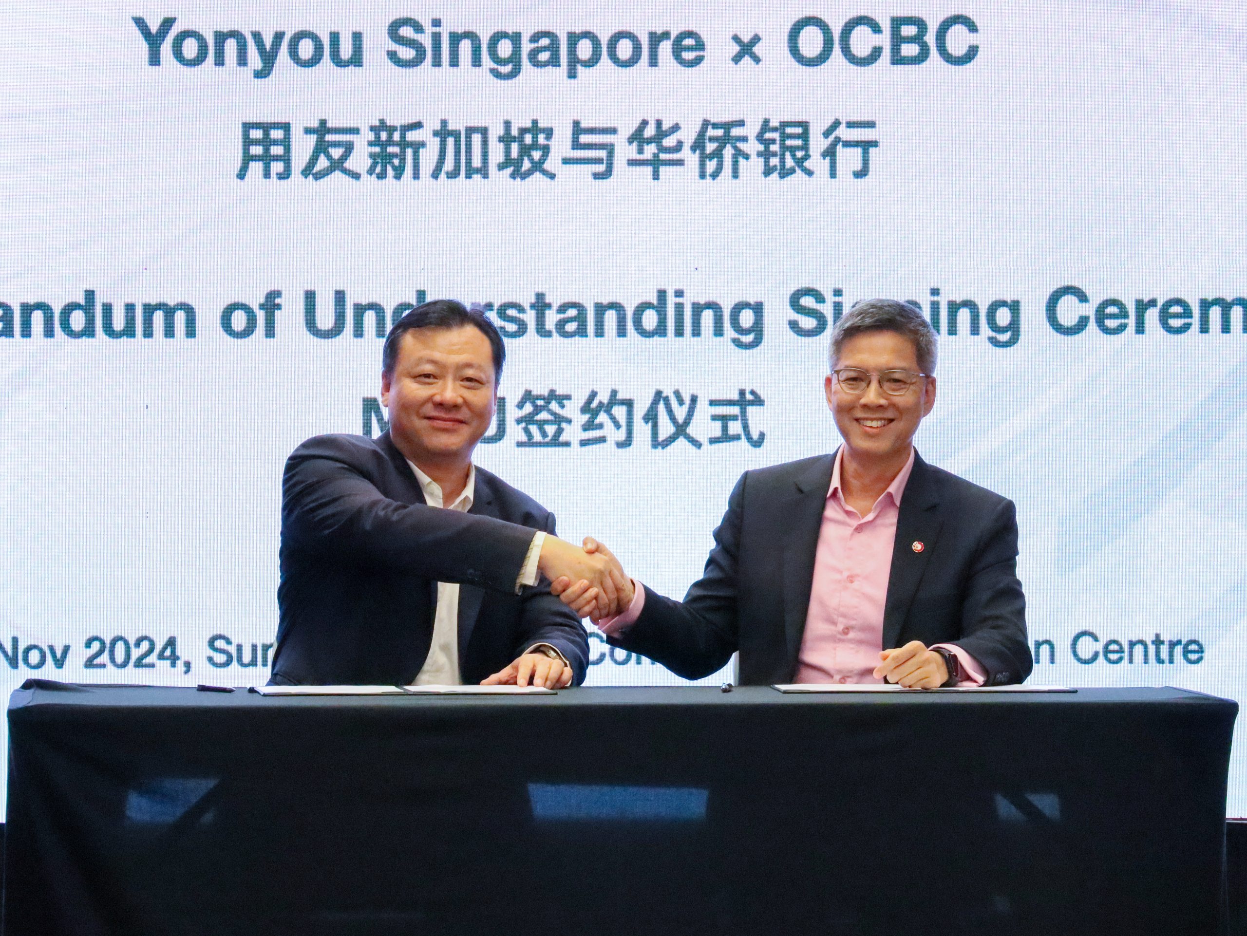 Howard Chen, Managing Director of Yonyou Network Technology (Singapore), and Roy Tan, Head of Enterprise Banking International, Global Commercial Banking, OCBC, shaking hands in a celebratory gesture following the successful collaboration, both smiling in agreement.