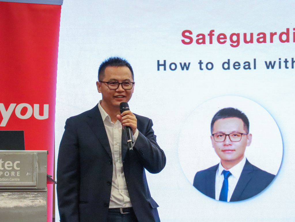 Tony Chen, Head of Product Development at Yonyou South Asia-Pacific, holding a microphone and addressing the audience on the critical importance of enterprise cybersecurity, with a presentation slide displayed in the background.
