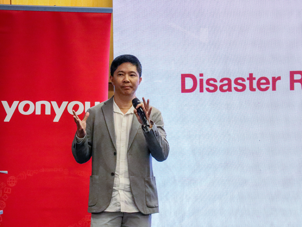 Roger Law, Regional Director of Revenue at Jumborca, speaking while highlighting the company's comprehensive data protection solutions. The background features Yonyou's logo on the left with a pull-up banner, and a PowerPoint slide displayed on the right.