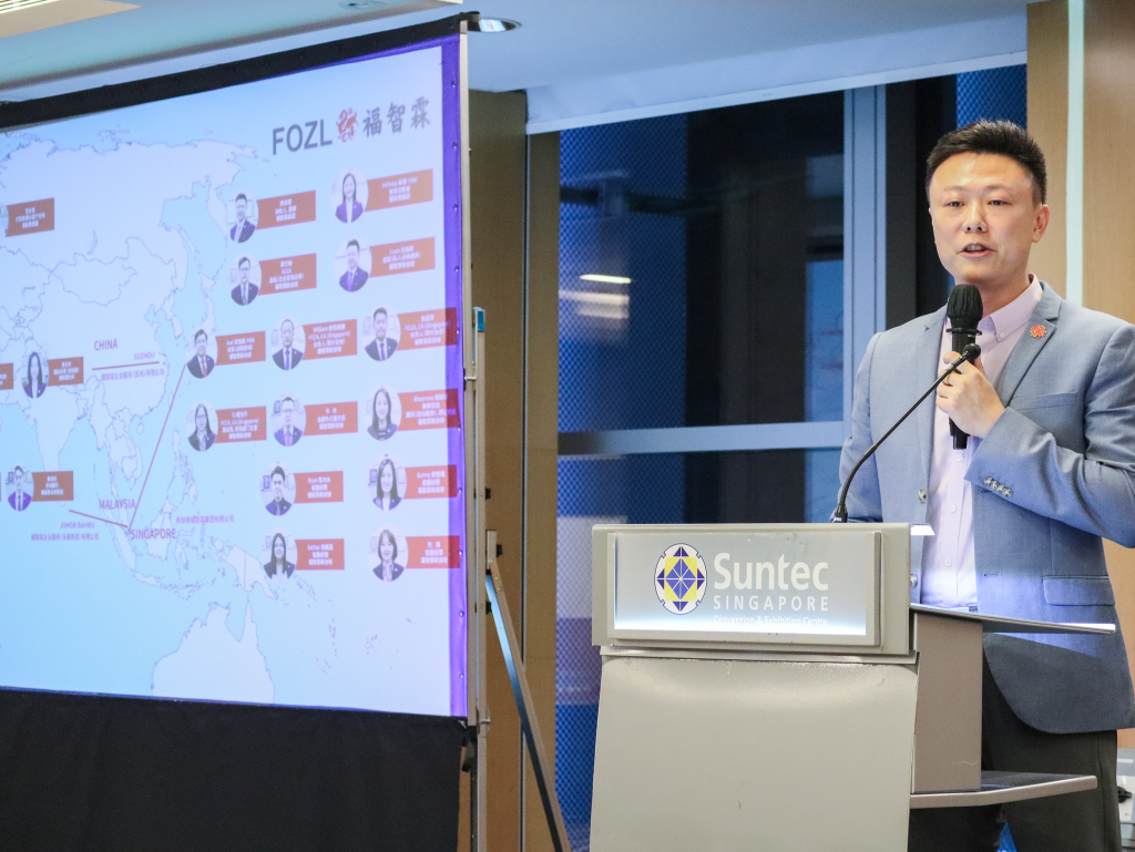 Huang Zelin, Group Director of FOZL, speaking at the Yonyou Customer Connect SEA 2024 event from the podium. On the left, a PowerPoint slide is displayed, detailing FOZL's successful implementation and ongoing use of Yonyou's financial and accounting system.
