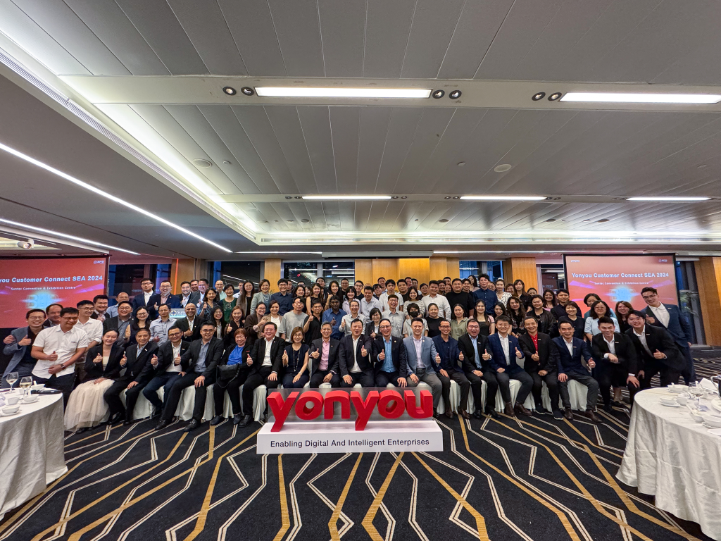 Group photo taken inside the venue, featuring a 3D Yonyou logo at the center with the tagline 'Enabling Digital and Intelligent Enterprise' displayed below. Dinner tables are set on both sides, indicating the photo was taken before the exclusive guest dinner.