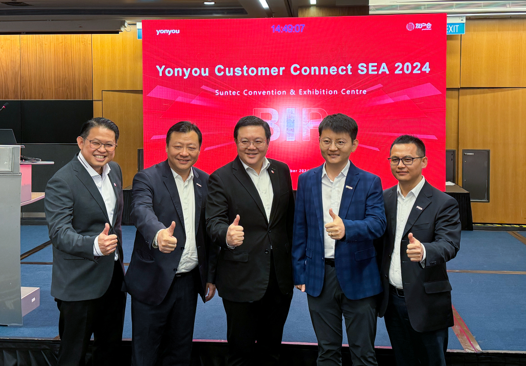 From left to right: Chong Hon Loon, Managing Director of Global Transaction Banking at OCBC Singapore; Howard Chen, Managing Director of Yonyou Network Technology (Singapore); Lim Chiang Fong, Managing Director of Enterprise Banking International at OCBC Bank; Bruce Xu, Managing Director of PT Yonyou Network Technology (Indonesia); and Tony Chen, Development Director of Yonyou Network Technology (Singapore), all smiling and giving a thumbs-up in front of a stage with a PowerPoint slide displaying the event title in the background.