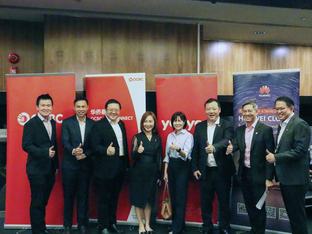 From left to right: Hari Purwanto, Vice President of Enterprise Banking International at OCBC Bank; San Shiuh Loon, Shaun, Business Head of China Business at Commercial Banking, OCBC Bank (Malaysia) Bhd; Lim Chiang Fong, Managing Director of Enterprise Banking International at OCBC Bank; Leong Pei Pei, Managing Director of Head China Business at OCBC Bank (Malaysia) Bhd; Goh Ai Mui, Lorraine, Executive Director of Enterprise Banking International at OCBC Bank; Howard Chen, Managing Director of Yonyou Network Technology (Singapore); Roy Tan, Head of Enterprise Banking International at Global Commercial Banking, OCBC Bank; Chong Hon Loon, Managing Director of Global Transaction Banking at OCBC Singapore, all smiling and giving a thumbs-up in front of several company banners.